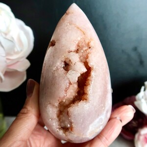 Puede incluir: Un cristal en forma de l&aacute;grima rosa y blanco con una gran geoda abierta en su interior. El cristal es liso y pulido, con una textura natural y rugosa en el interior de la geoda.
