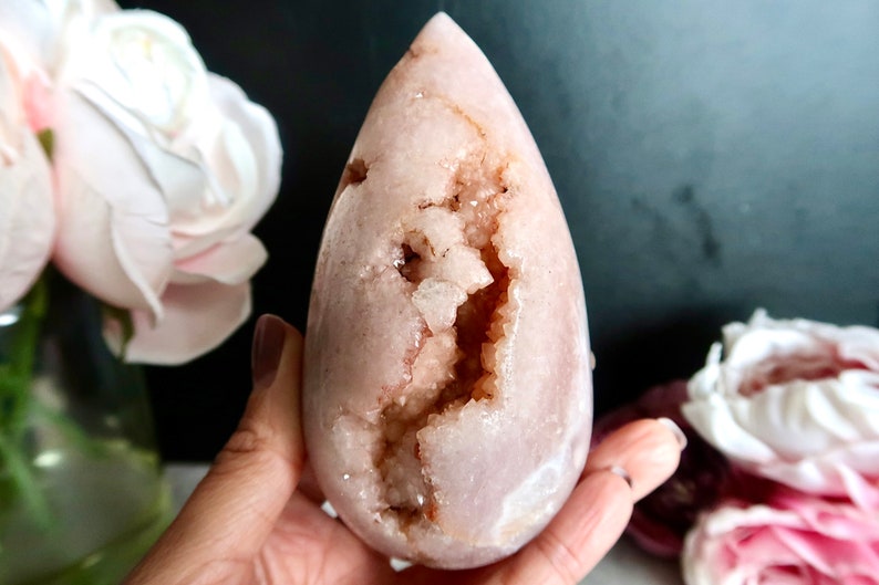 Puede incluir: Un cristal en forma de l&aacute;grima rosa y blanco con una gran geoda abierta en su interior. El cristal es liso y pulido, con una textura natural y rugosa en el interior de la geoda.