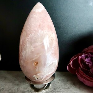 Puede incluir: Un cristal de forma de l&aacute;grima rosa y blanco sobre un soporte plateado. El cristal tiene una superficie lisa y pulida y una forma natural y org&aacute;nica.