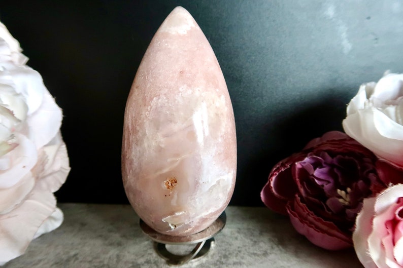 Puede incluir: Un cristal de forma de l&aacute;grima rosa y blanco sobre un soporte plateado. El cristal tiene una superficie lisa y pulida y una forma natural y org&aacute;nica.