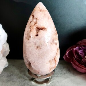 Puede incluir: Un cristal de forma de l&aacute;grima rosa y blanco sobre un soporte plateado. El cristal tiene una superficie rugosa y texturizada.