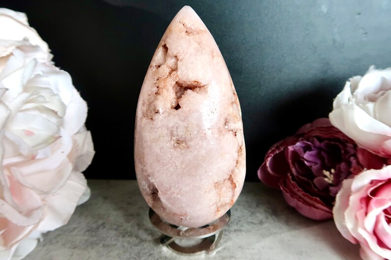 Puede incluir: Un cristal de forma de l&aacute;grima rosa y blanco sobre un soporte plateado. El cristal tiene una superficie rugosa y texturizada.