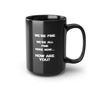 May include: Black ceramic coffee mug with white text that reads "We're fine. We're all fine here now... How are you?"