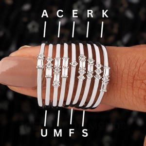 Könnte beinhalten: Eine Sammlung von Diamantringen mit abwechselnd schwarzen und weißen Bändern. Jeder Ring ist mit einer Reihe kleiner, funkelnder Diamanten besetzt. Die Ringe werden an einem Finger präsentiert, um das Design und die Details des Schmucks hervorzuheben.