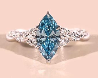 May include: A marquise-cut, light blue gemstone ring with a silver band. The ring features a large central stone and smaller accent stones. The band has a twisted design. The ring is set against a soft pink background.