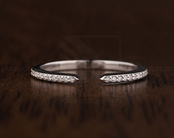Pode incluir: Um delicado anel de prata com uma fileira de pequenos diamantes engastados em uma banda contínua. O anel é aberto de um lado, criando um design único e moderno.