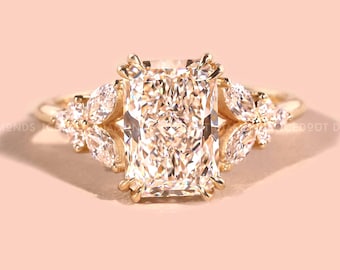 May include: A radiant-cut diamond ring with a gold band. The center stone is a large, rectangular diamond, flanked by smaller, pear-shaped diamonds. The ring is set against a soft pink background, creating a luxurious and elegant aesthetic.
