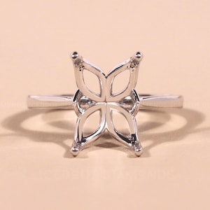 May include: A silver ring with a butterfly-shaped setting. The ring's design features four open, petal-like shapes forming the butterfly. The band is a simple, polished silver. The ring is set against a neutral background.