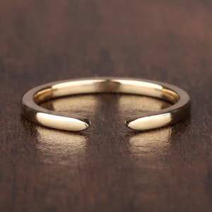 May include: A simple gold ring with a rounded, slightly curved shape. The ring is open on one side, making it adjustable.