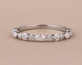 Puede incluir: Un delicado anillo de plata con una serie de piedras preciosas claras de corte redondo y marquesa. Las piedras están espaciadas uniformemente alrededor de la banda, creando un diseño brillante y elegante. Fondo neutro.