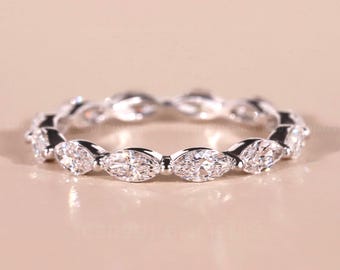 Puede incluir: Un anillo de plata con una banda continua de diamantes talla marquesa. Los diamantes están engastados muy juntos, creando un diseño brillante y elegante. El anillo se muestra sobre una superficie neutra y clara.