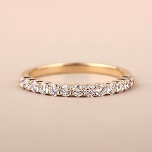 May include: A gold band ring set with a row of clear, round-cut diamonds. The ring is displayed on a neutral background, showcasing the sparkle of the gemstones. The ring is a classic style, suitable for various occasions.