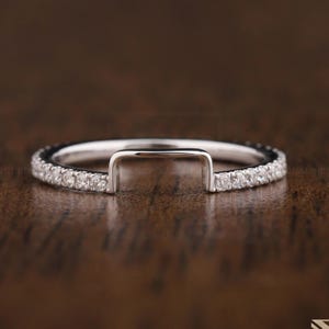 Puede incluir: Un delicado anillo de oro blanco con una abertura en forma de U y una fila de pequeños diamantes brillantes alrededor de la banda.