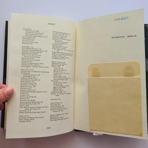 Pu&ograve; includere: Libro aperto che mostra una pagina indice con un elenco di argomenti e numeri di pagina. Una tasca color beige chiaro &egrave; visibile sulla pagina di destra. Il libro &egrave; aperto, rivelando l'indice e una tasca. Il dorso del libro &egrave; nero.