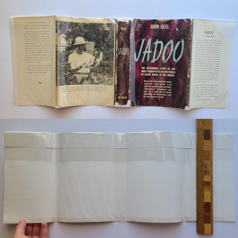 May include: An open book titled "Jadoo" by John Keel, with a dark red cover and the text "The Astounding Story of One Man's Search into the Mysteries of Black Magic in the Orient." The book is open to reveal interior pages with text and a black and white photograph. A wooden ruler is visible.