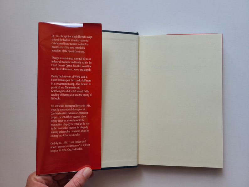 Puede incluir: Un libro rojo con una columna vertebral blanca y una p&aacute;gina blanca abierta para revelar una p&aacute;gina en blanco. La portada del libro tiene texto sobre Franz Bandon, un adepto herm&eacute;tico, y su vida y obra.