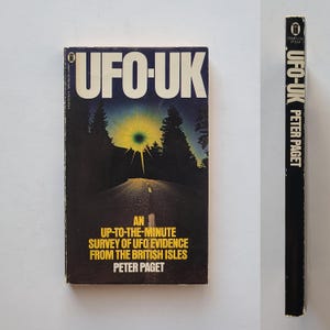 May include: A black and white book cover with the title "UFO-UK" in large white letters. The book cover features a photo of a road through a forest with a bright light in the sky. The book subtitle is "An Up-to-the-Minute Survey of UFO Evidence from the British Isles" and the author is Peter Paget.