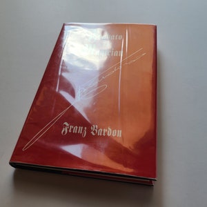Puede incluir: Un libro de tapa dura rojo con un t&iacute;tulo y un nombre de autor blancos. El t&iacute;tulo es "Initiato en Magia" y el autor es "Franz Bardon".