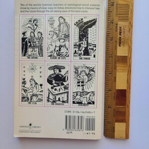 Puede incluir: Un libro de bolsillo vintage con ilustraciones de cartas del tarot. La contraportada muestra seis cartas del tarot, incluyendo "Los Amantes" y "El Mago". Una regla de madera est&aacute; al lado del libro, mostrando medidas en cent&iacute;metros. El t&iacute;tulo del libro es visible.