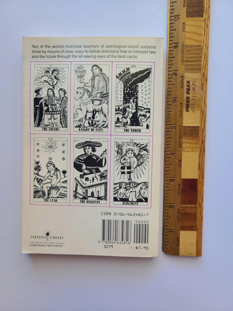 Puede incluir: Un libro de bolsillo vintage con ilustraciones de cartas del tarot. La contraportada muestra seis cartas del tarot, incluyendo "Los Amantes" y "El Mago". Una regla de madera est&aacute; al lado del libro, mostrando medidas en cent&iacute;metros. El t&iacute;tulo del libro es visible.