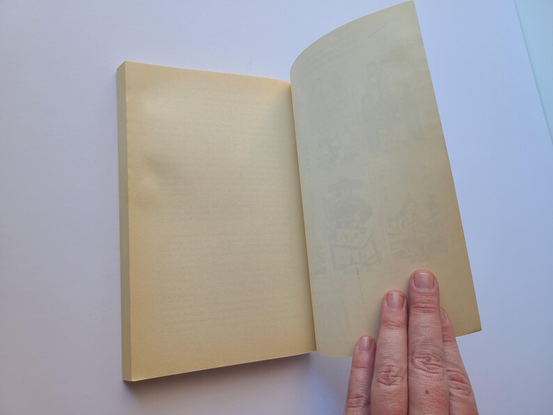 Puede incluir: Un libro abierto con p&aacute;ginas amarillentas. El lado izquierdo est&aacute; cerrado, el derecho abierto, revelando ilustraciones tenues. Una mano sostiene las p&aacute;ginas abiertas.