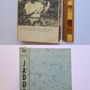 May include: Vintage book titled "Jadoo" by Keel. The cover is light blue with a marbled pattern and the spine reads "Jadoo" vertically. The book's cover has a photo of a person handling a snake. A wooden ruler is next to the book.