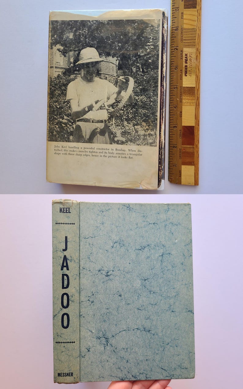 May include: Vintage book titled "Jadoo" by Keel. The cover is light blue with a marbled pattern and the spine reads "Jadoo" vertically. The book's cover has a photo of a person handling a snake. A wooden ruler is next to the book.