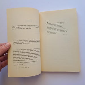 Puede incluir: Libro abierto con texto en las p&aacute;ginas. El libro se titula "How to Read Tarot Cards". Las p&aacute;ginas son de color crema con texto negro. El libro est&aacute; abierto, revelando texto y una mano que sostiene el libro.