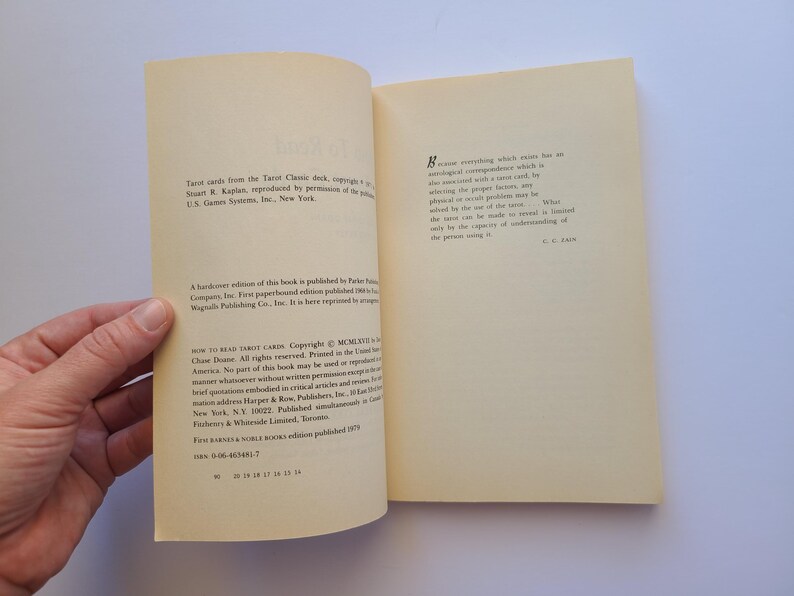 Puede incluir: Libro abierto con texto en las p&aacute;ginas. El libro se titula "How to Read Tarot Cards". Las p&aacute;ginas son de color crema con texto negro. El libro est&aacute; abierto, revelando texto y una mano que sostiene el libro.