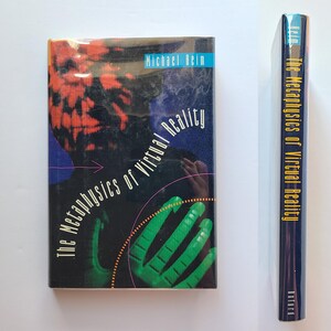 May include: A book titled "The Metaphysics of Virtual Reality" by Michael Heim. The cover features a dark background with a red and black abstract design, a green hand, and the title in white. The spine is visible, showing the title and the Oxford logo.