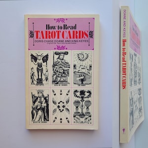 Puede incluir: Un libro antiguo titulado "How to Read Tarot Cards" de Doris Chase Doane y King Keyes. La portada presenta un fondo rosa con el t&iacute;tulo en negrita e ilustraciones de cartas del tarot. El lomo del libro tambi&eacute;n es visible.