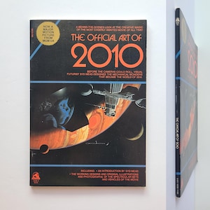 May include: The Official Art of 2010 book. The cover features a space scene with planets, a spaceship, and a figure in a spacesuit. The book includes an introduction by Syd Mead and illustrations of the movie's sets and vehicles.