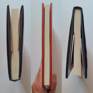 Puede incluir: Tres vistas diferentes de un libro de tapa dura con una columna vertebral roja y una sobrecubierta azul marino. El libro est&aacute; cerrado y de pie.