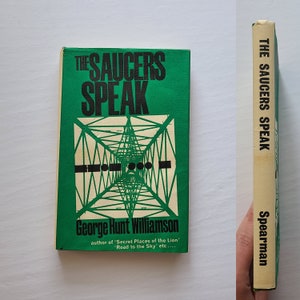 May include: A green book cover with the title "The Saucers Speak" in black text. The author is George Hunt Williamson, and the book is published by Spearman.