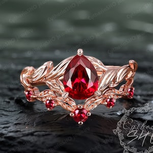 Peut inclure: Une bague en or rose avec une pierre précieuse en rubis de forme poire, entourée de détails délicats en forme de feuilles et de petits accents en rubis.