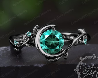 May include: Black ring with a crescent moon design and a large, round, teal gemstone. The ring is adorned with delicate, leafy details and smaller gemstones.