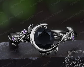 May include: A silver ring with a black gemstone set in a crescent moon design. The ring is adorned with delicate silver branches and purple gemstones.