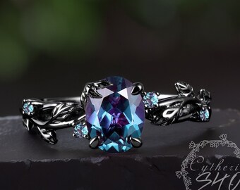 May include: A black ring with an oval, color-changing gemstone. The ring features a leaf design on the band and small blue accent stones. The gemstone shifts between blue and purple hues, set against a dark background.