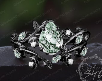 May include: A black ring with a green and white gemstone set in a vine design. The ring is accented with small white gemstones.