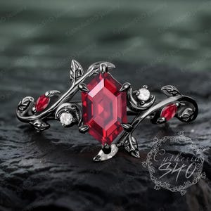 May include: A black ring with a large, red, hexagonal gemstone surrounded by smaller, white gemstones. The ring features a delicate, vine-like design with leaves and branches.