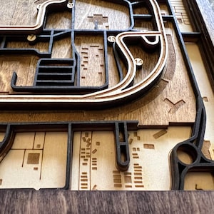 May include: A wooden 3D map with a layered design, featuring a city layout with streets and buildings. The map is made of dark brown wood and has a light brown wood background.