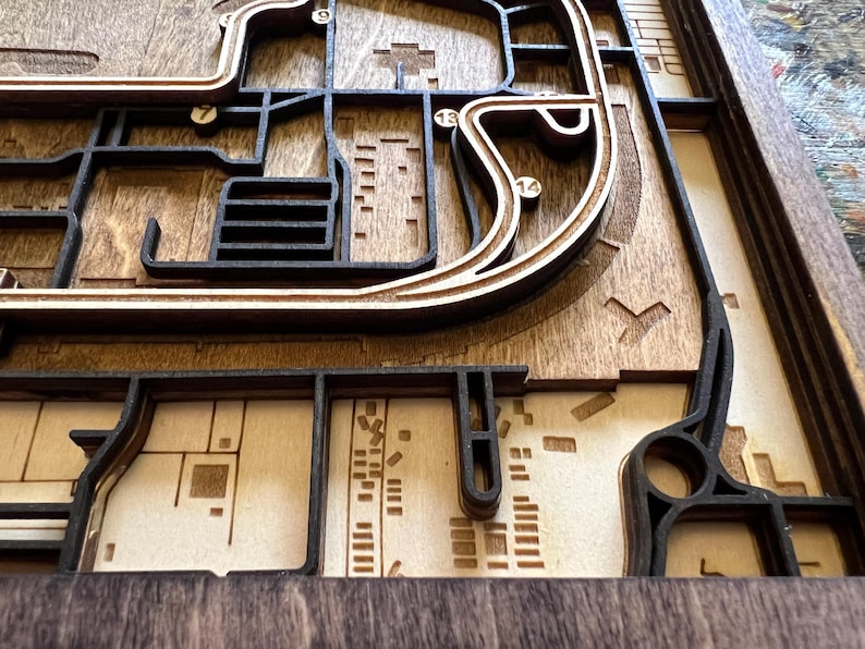 May include: A wooden 3D map with a layered design, featuring a city layout with streets and buildings. The map is made of dark brown wood and has a light brown wood background.