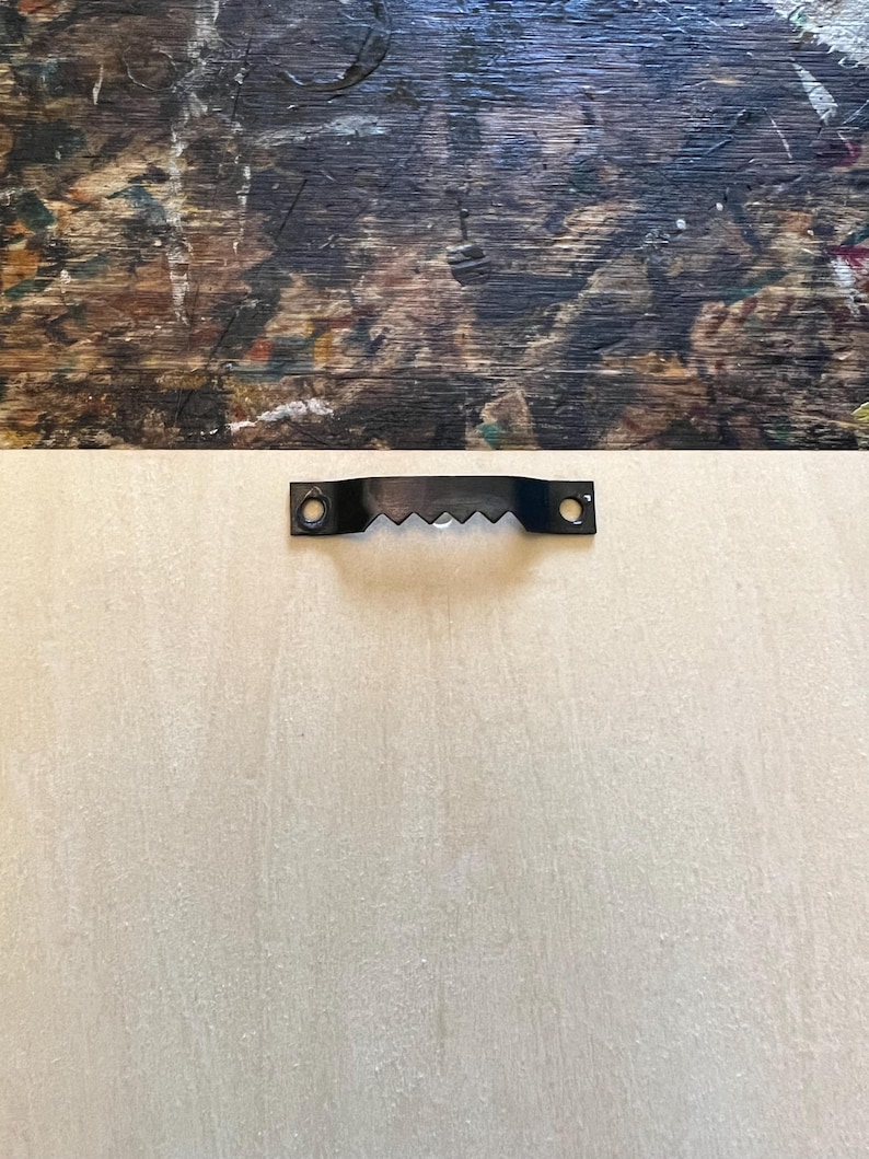 May include: A close-up of a light beige wooden surface with a black metal hanging hook attached to the top.