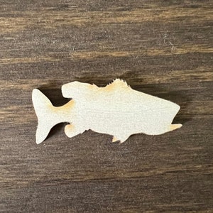 May include: A wooden cutout of a fish in a light brown color. The fish is facing right and has a slightly curved body.