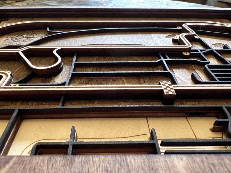May include: A wooden race track model with a checkered flag finish line. The track is made of dark wood and has a light wood border. The track is raised off the surface and has a 3D effect.