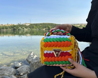 May include: A colorful crocheted handbag with a gold chain strap. The bag is made of different colored yarn, including yellow, orange, green, red, and white. The bag has a unique design and is perfect for everyday use.