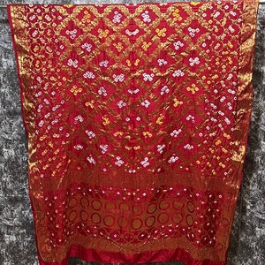 May include: A red, gold, and white patterned silk saree with a traditional design. The saree has a border with a repeating circle pattern.