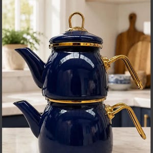 Pode incluir: Um conjunto de chaleira de dois níveis com acabamento em esmalte azul-marinho profundo e alças, bicos e detalhes da tampa em metal dourado polido. O design empilhado apresenta uma chaleira superior menor com tampa e uma base maior.