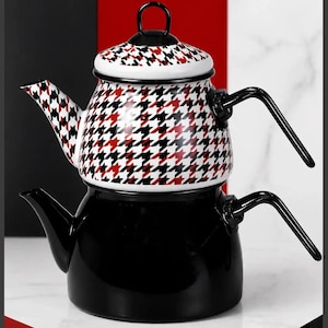 Pode incluir: Um conjunto de bule de duas peças com uma base preta sólida e uma parte superior decorada com um padrão pied-de-poule em vermelho, branco e preto. Ambas as peças possuem alças e bicos pretos, com uma tampa a condizer no topo.