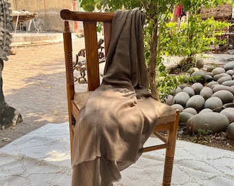 May include: A brown throw blanket draped over a wooden chair with a carved back and turned legs. The chair is sitting on a white rug with a diamond pattern.